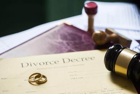 wedding rings and a gavel sit on top of a divorce decree